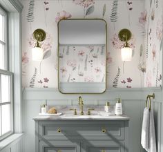 a bathroom with floral wallpaper and gold faucet lights on the mirror above the double sink