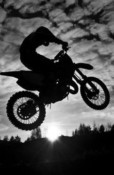 a person on a dirt bike doing a trick in the air with the sun behind them