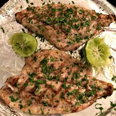 two pieces of chicken on tin foil with limes