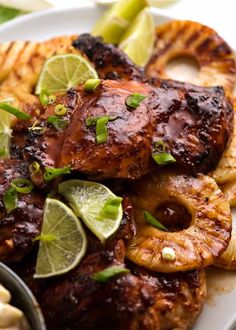 grilled chicken and pineapples on a white plate with lime wedges next to them