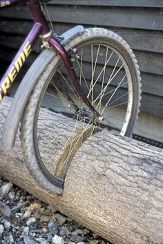 an old bicycle is parked on a log in front of a wooden building with the wheel missing