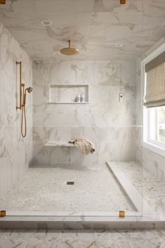 a bathroom with white marble walls and floor, gold fixtures on the shower head and shelf