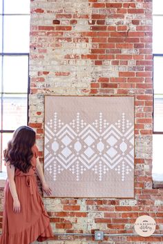 a woman standing in front of a brick wall with a quilt hanging on the wall