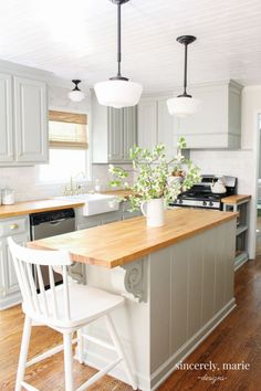 a kitchen island with two white chairs next to it and a potted plant on the counter