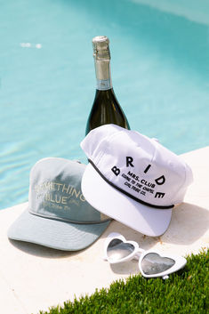 a bottle of wine and sunglasses sitting on the edge of a pool next to a hat