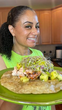 a woman holding a green plate with food on it and smiling at the camera,