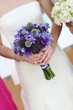 two brides holding bouquets of purple and white flowers in their hands while standing next to each other