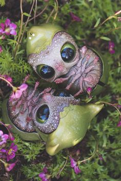 two green vases with blue eyes are sitting in the middle of purple and pink flowers