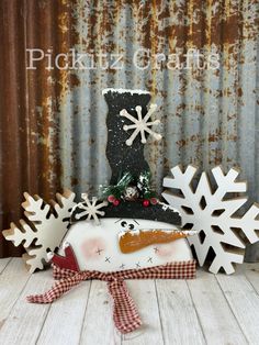 a snowman made out of wood sitting on top of a wooden table next to some snowflakes