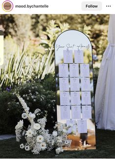 a wedding seating chart with white flowers in the foreground and an outdoor ceremony backdrop