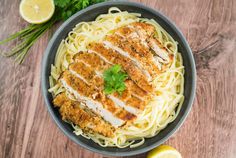 a bowl filled with chicken and pasta on top of a wooden table next to lemon wedges