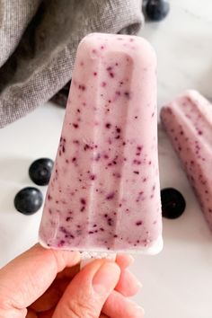 a hand holding an ice cream bar with blueberries on the table next to it