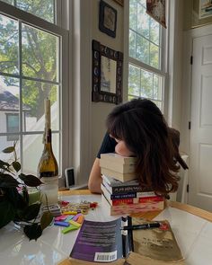 a woman sitting at a table with books on top of her head in front of a window