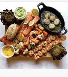 a wooden cutting board topped with different types of food next to dipping sauces and artichokes