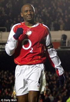 a man standing on top of a soccer field wearing a red and white uniform with his hands in his pockets