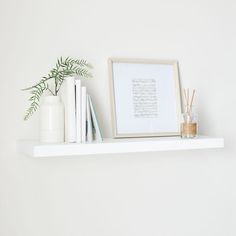 a white shelf with books, vases and plants on it next to a framed photograph