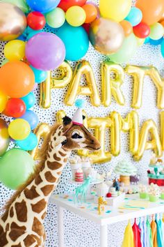 a giraffe standing in front of a party table with balloons and streamers