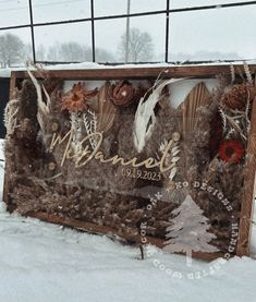 a wooden sign with feathers and pine cones on it in the snow next to a wire fence