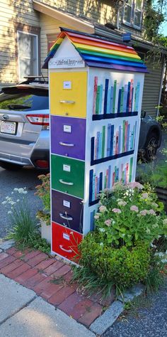 a multicolored bookcase is on the sidewalk next to some flowers and cars