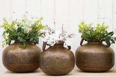 three vases with flowers in them sitting on a table next to each other,