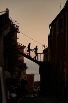 two people walking across a bridge over water at sunset or dawn with the sun setting in the background