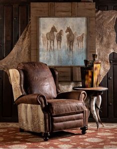 a brown chair sitting in front of a painting on a wall next to a table