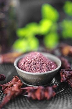 a metal bowl filled with purple powder on top of a black table cloth next to green plants