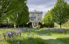 a large house surrounded by trees and flowers in the middle of a grassy area with a path leading to it