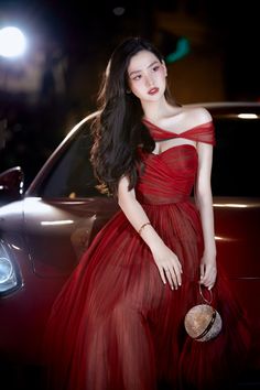 a woman in a red dress standing next to a car