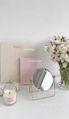 a table topped with a vase filled with white flowers and a mirror next to a candle