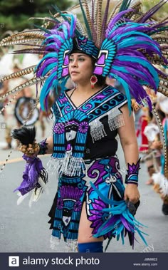 a woman in an elaborate costume walking down the street with feathers on her head and hands