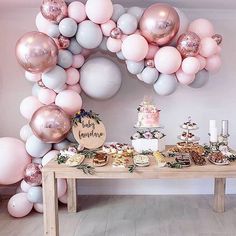 a table topped with lots of pink and white balloons next to a wall filled with cake