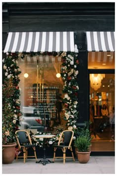 two chairs and a table in front of a store with flowers on the window sill