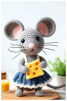 a crocheted mouse with a piece of cheese in it's hand, on top of a table