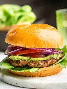 a burger with lettuce, tomato and onion on a marble plate next to a glass of green juice