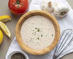 a wooden bowl filled with white sauce next to lemons, tomatoes and other ingredients