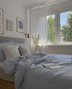 a bed with blue sheets and pillows in a bedroom next to a large window on the wall