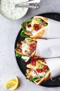 three pita wraps on a black plate with lemon wedges next to the wrappers