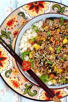 a bowl filled with rice and meat on top of a colorful table cloth next to chopsticks