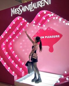 a woman standing in front of a pink display with lights on it's sides