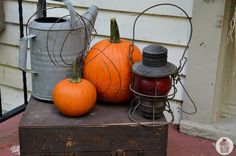 three pumpkins are sitting on top of an old trunk with a metal watering can next to it