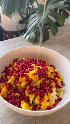 a white bowl filled with fruit sitting on top of a table next to a plant