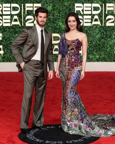 a man and woman standing on a red carpet in front of a wall with letters