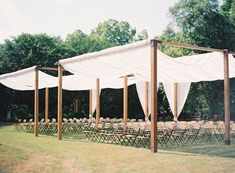 an outdoor wedding setup with white draping and wooden poles for the ceremony area