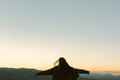 a woman standing on top of a hill with her arms spread out in the air