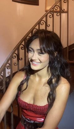 a beautiful young woman in a red dress standing next to a stair case and smiling