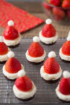 some cupcakes with santa hats on them are sitting on a cooling rack next to strawberries