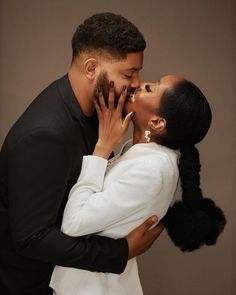 a man and woman kissing each other in front of a brown wall with their hands on her face