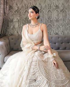 a woman sitting on top of a couch wearing a white dress and pearls in her hair