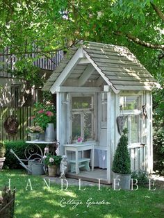 a small white shed sitting on top of a lush green field next to a tree